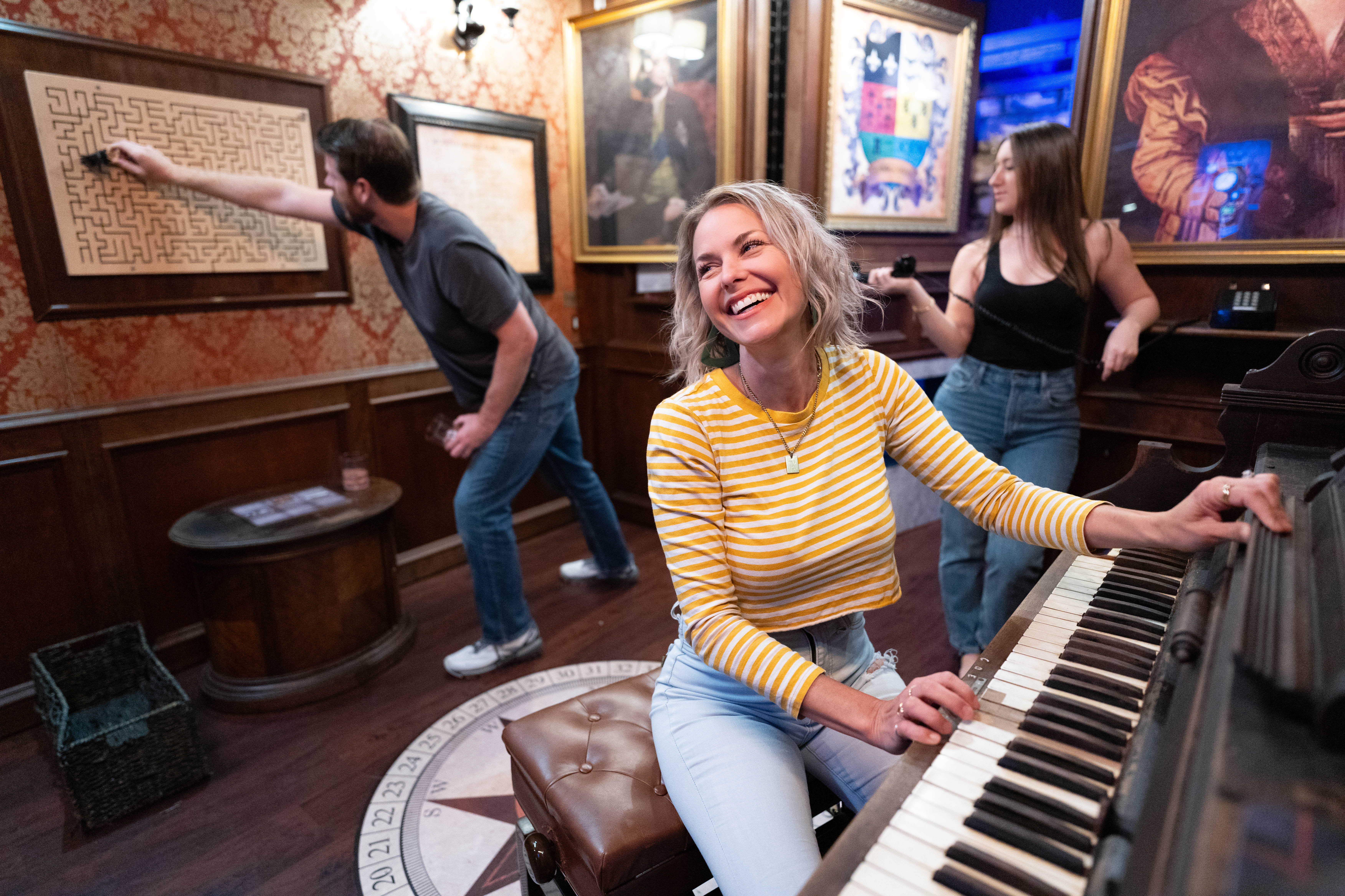 3 escape room players in a scottish mansion escape room with a piano, phone, and maze puzzle on the wall