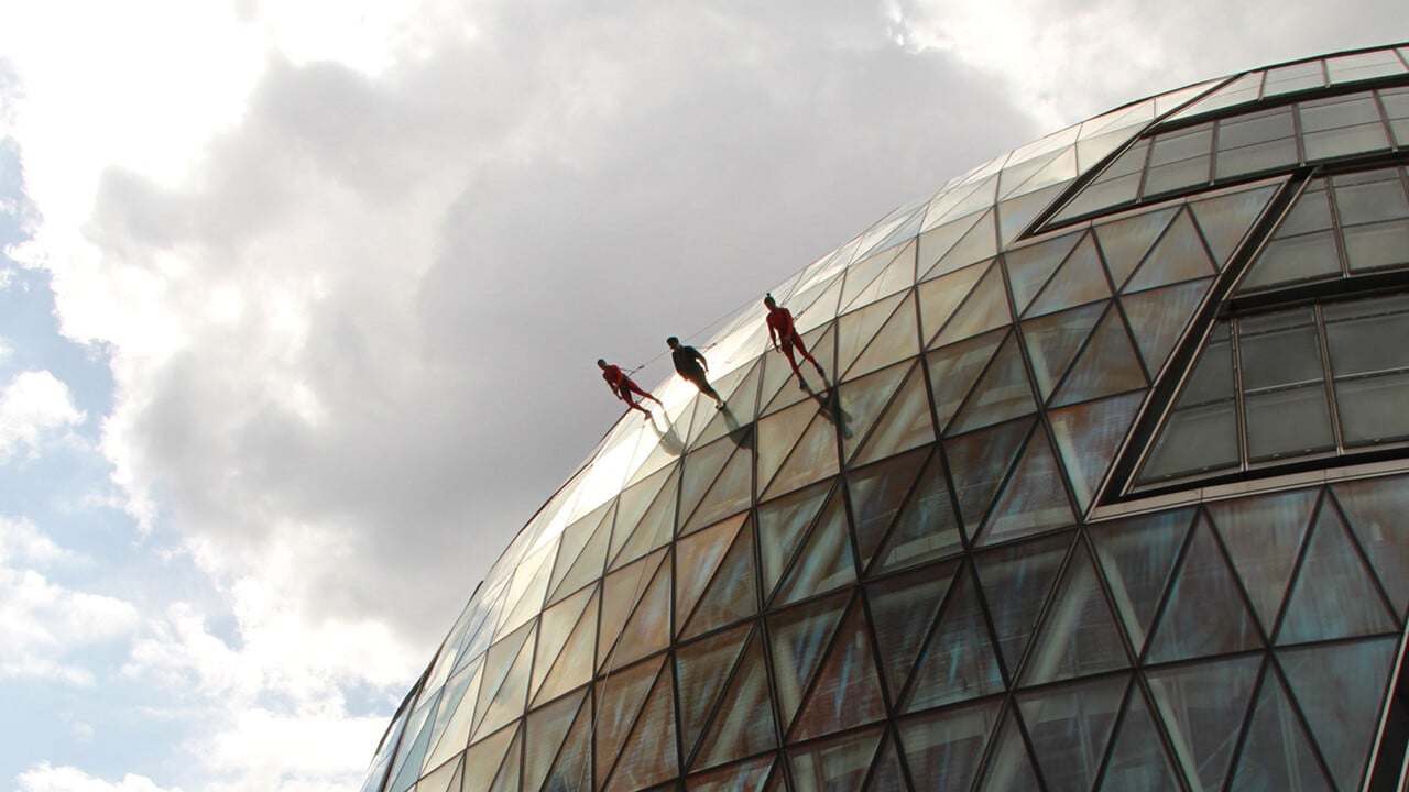 Three dancers walking along the side of a building, as part of a performance.