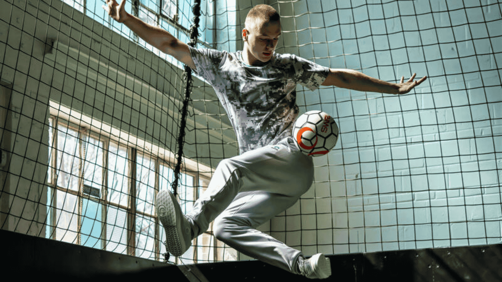 A white male mid air kicking a soccer ball in front of a goal post.