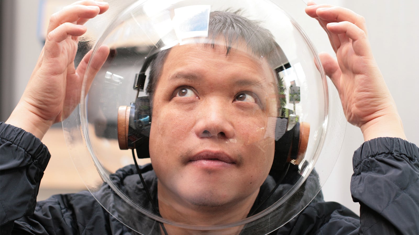 A young boy wearing over the ear headphones and a plastic astronaut helmet.