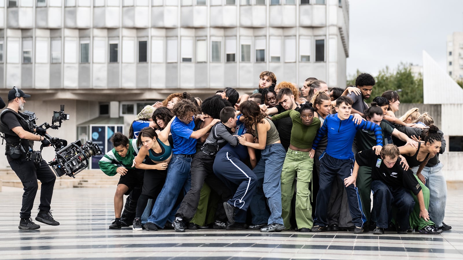 A group of dancers form a huddle with a camera man films them with a large camera.