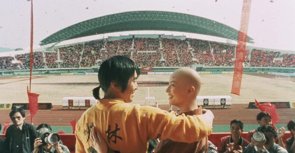 A man and a women embrace each other in front of a camera in a full stadium.